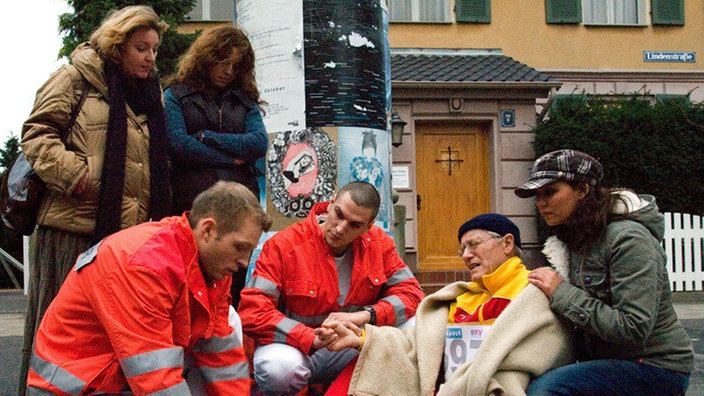 Das frühzeitige Ende des Stadtlaufs: Hans (Joachim Hermann Luger) hat sich den Fuß verknackst und muss in ärztliche Behandlung. "Trainerin" Kathy (Sabine Pfeifer) ist besorgt.