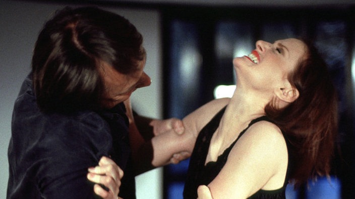 Dabelstein (Thomas Frey) nötigt die völlig verzweifelte Anna (Irene Fischer), sein "Geschenk" sofort anzuziehen. Doch dann beginnt Anna, sich zu wehren...