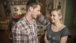 Daniel und Lea lächeln sich vor der essenden Familie stehend an