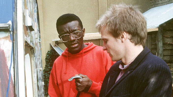 David (Ronald Mkwanazi, links) hilft Zorro (Thorsten Nindel), den von Faschos demolierten Wohnwagen zu reparieren.