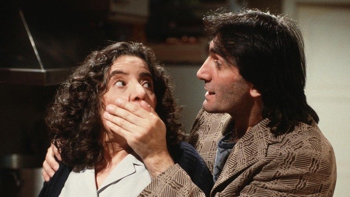 Dimitri (Roberto Eftimiades) verhindert einen Streit mit seiner Schwester Elena (Domna Adamopoulou) indem er ihr den Mund zuhält.