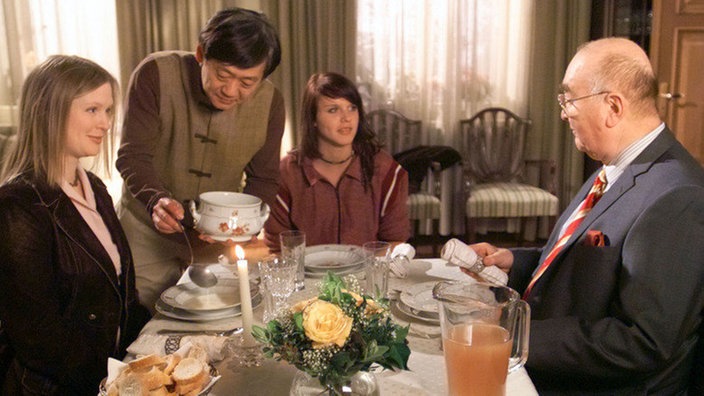 Dressler (Ludwig Haas, rechts) hat seine Ex-Frau Tanja (Sybille Waury, links) zum Abendessen mit Jack (Cosima Viola) eingeladen. Gung (Amorn Surangkanjanajai) staunt und serviert.