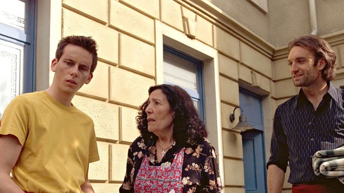 Elena (Domna Adamopoulou) ist besorgt, Julian (Urs Villiger, rechts) nimmt das Ganze nicht ernst: Fabian (Roman Haubner) hat einen herrenlosen Koffer im Biergarten des “Akropolis” entdeckt.