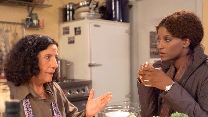 Elena (Domna Adamopoulou, links) bittet Mary (Liz Baffoe) um Verständnis für Vasilys harsches Verhalten.