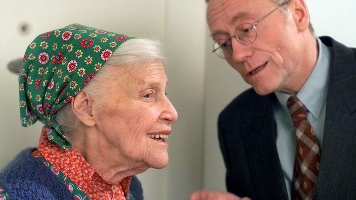Else (Annemarie Wendl) möchte von Hans (Joachim Hermann Luger) wissen, was es mit der geheimnisvollen Feier im Hause Beimer-Ziegler auf sich hat.