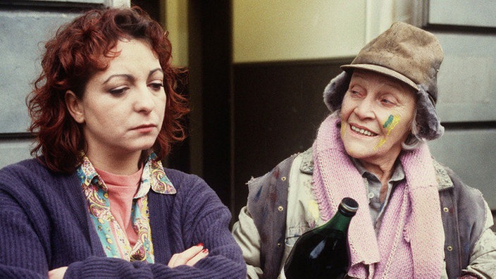 Else (Annemarie Wendl, rechts), die sich weiterhin als Malerin verdingt, erzählt Claudia (Manon Straché) Lügenmärchen wegen der geplanten Hochzeitsreise.