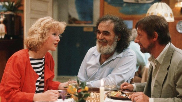 Franz (Raimund Gensel, rechts) und Tanja (Sybille Waury) begießen ihre Rückkehr mit Panaiotis (Kostas Papanastasiou) im "Akropolis".