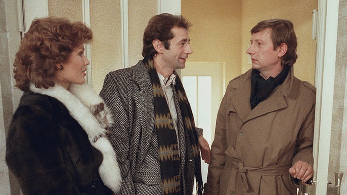 Franz Schildknecht (Raimund Gensel, rechts) weiß noch nicht recht, was er von dem Verhalten seiner Frau Henny (Monika Woytowicz) halten soll. Gerade erklärt sie ihm, dass sie mit Stefan Nossek (Dietrich Siegl) Tanja abholen will.