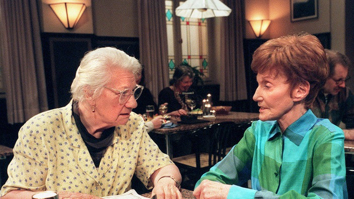 Frau Birkhahn (Hanna Burgwitz, li) und Rosi (Margret van Munster) setzen ihre Arbeit am Kreuzworträtsel fort.