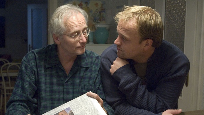 Hans (Joachim Hermann Luger, links) ist stolz auf Klaus (Moritz A. Sachs). Der hat in der Zeitung einen Artikel platzieren können, mit dem die Familie Beimer-Ziegler rehabilitiert wird.