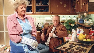Hans (Joachim Hermann Luger) spült seine beruflichen Ängste bei Helga (Marie-Luise Marjan) herunter und wird Zeuge, wie die Weihnachtsplätzchen einmal mehr zu "schwarzen Raben" mutieren.