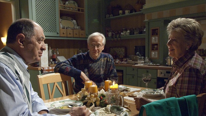 Hans (Joachim Luger, Mitte) ist erstaunt, dass sich Helga (Marie-Luise Marjan) und Professor Melchior (Jürgen Haug) beim Abendessen so vertraut sind.