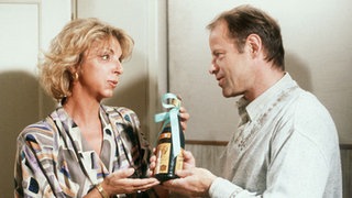 Hans-Joachim Scholz (Knut Hinz) überrascht Berta Griese (Ute Mora) mit einem Geschenk.
