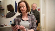 Hans steht hinter Anna, die auf ein Handy schaut