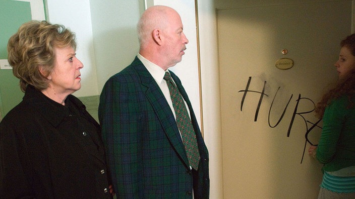 Helga (Marie-Luise Marjan, links) und Erich (Bill Mockridge) sind entsetzt: Nastya (Anja Antonowicz) wird mit der Schmiererei als „Hure“ beschimpft.