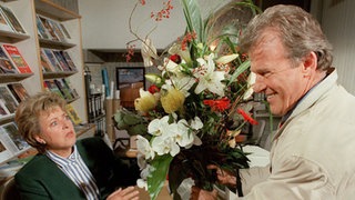 Helgas (Marie-Luise Marjan) Dauer-Verehrer Lösch (Wichart von Roell) erscheint mit Blumen in der Hand und Komplimenten auf den Lippen.