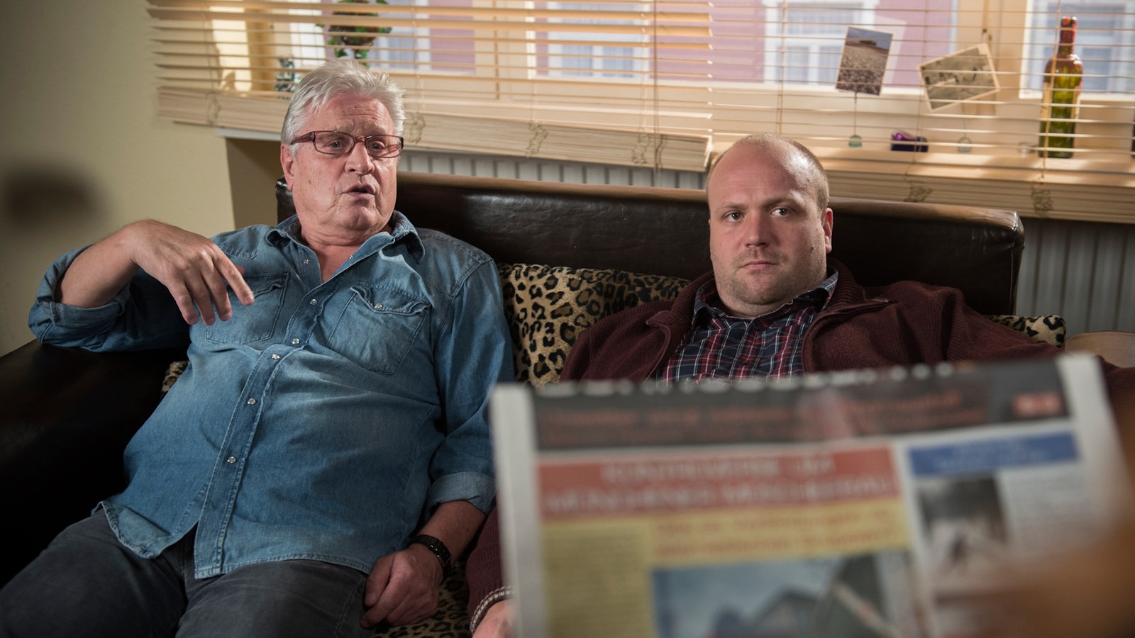 Iffi diskutiert eine Zeitung haltend mit Klaus und Andy