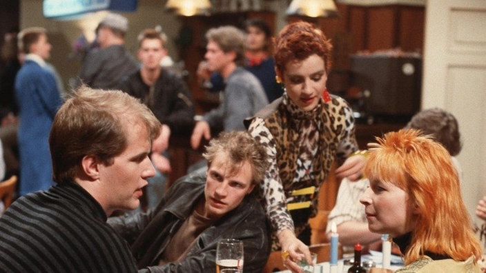Im "Akropolis" besprechen Carsten (Georg Uecker, links), Zorro (Thorsten Nindel) und Chris (Stefanie Mühle, rechts) ihre Klebe-Aktion, während Beate (Susanne Gannott) sie mit Getränken versorgt.