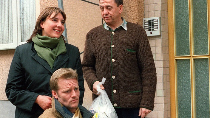 Ines (Birgitta Weizenegger) kümmert sich gern um ihren verletzten Ex-Gatten Ingo (Holger Doellmann, links). Olaf (Franz Rampelmann), der neue Mann an Ines' Seite, beobachtet das Ganze argwöhnisch.