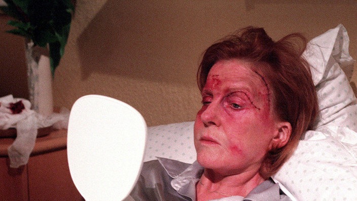 Isolde (Marianne Rogée) hat sich von der Schwester einen kleinen Spiegel geben lassen um das Resultat der Schönheitsoperation zu begutachten: Sie ist entsetzt.