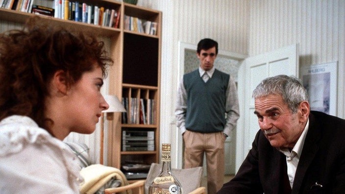 Joschi (Herbert Steinmetz, rechts) erkundigt sich bei Kronmayrs (Claudia Pielmann, Franz Braunshausen) nach dem Verbleib der kostbaren Bibel.