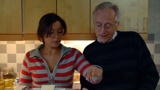 Kathy (Sabine Pfeifer) fängt heute als Hausmädchen an und erklärt Hans (Joachim Hermann Luger) wie sie sich die Arbeitsaufteilung vorstellt.