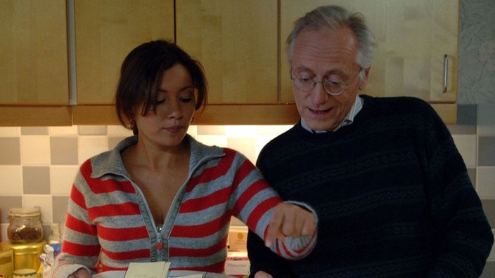 Kathy (Sabine Pfeifer) fängt heute als Hausmädchen an und erklärt Hans (Joachim Hermann Luger) wie sie sich die Arbeitsaufteilung vorstellt.