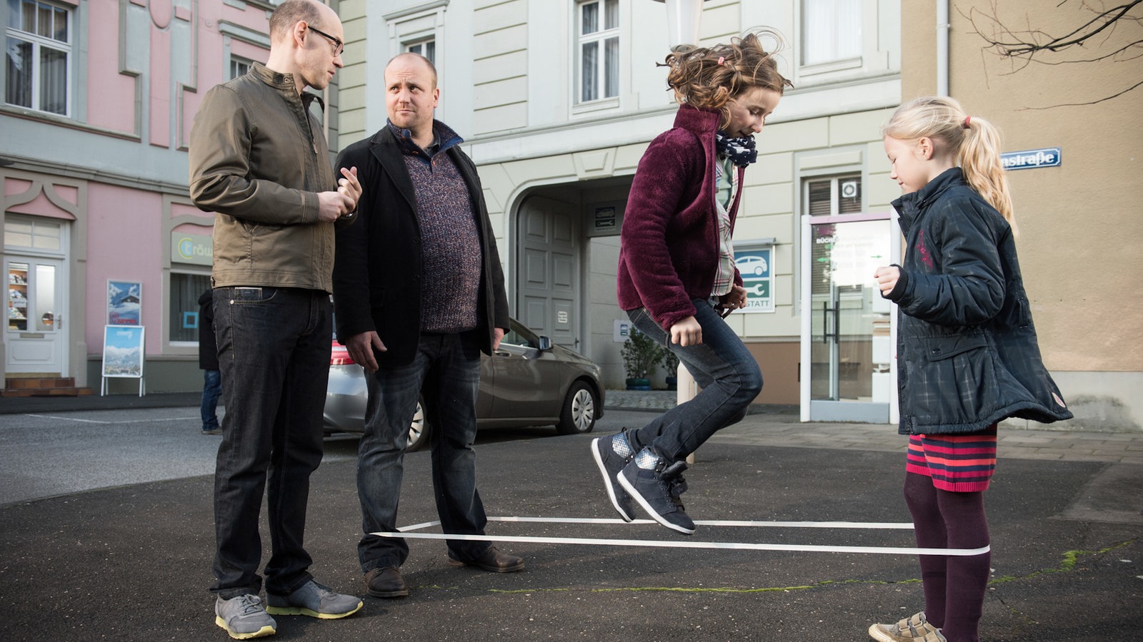 Klaus, Mila und Antonia spielen Gummitwist, Philipp steht daneben