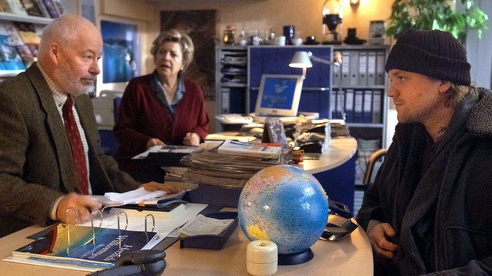 Klaus (Moritz A. Sachs, rechts) erkundigt sich bei Erich (Bill Mockridge) über Reisemöglichkeiten ins südliche Afrika. Helga (Marie-Luise Marjan) mag kaum ihren Ohren trauen.
