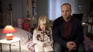 Klaus sitzt mit Mila auf einem Bett