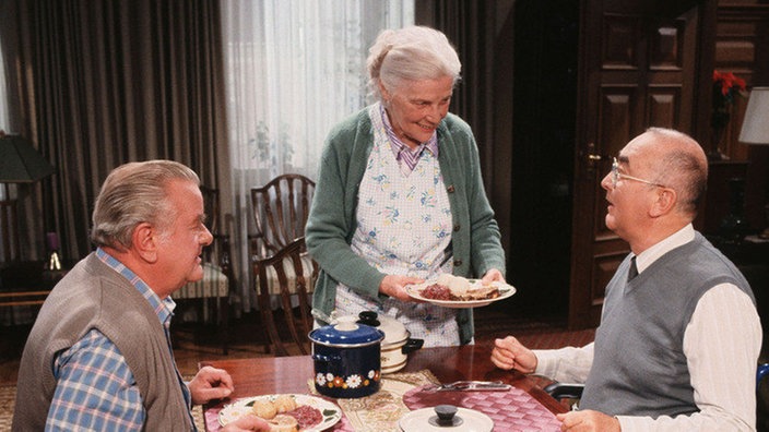 Kochduell: Wer macht den besseren Schweinebraten - Else (Annemarie Wendl) oder Egon (Wolfgang Grönebaum, links)? Dressler (Ludwig Haas) soll entscheiden.