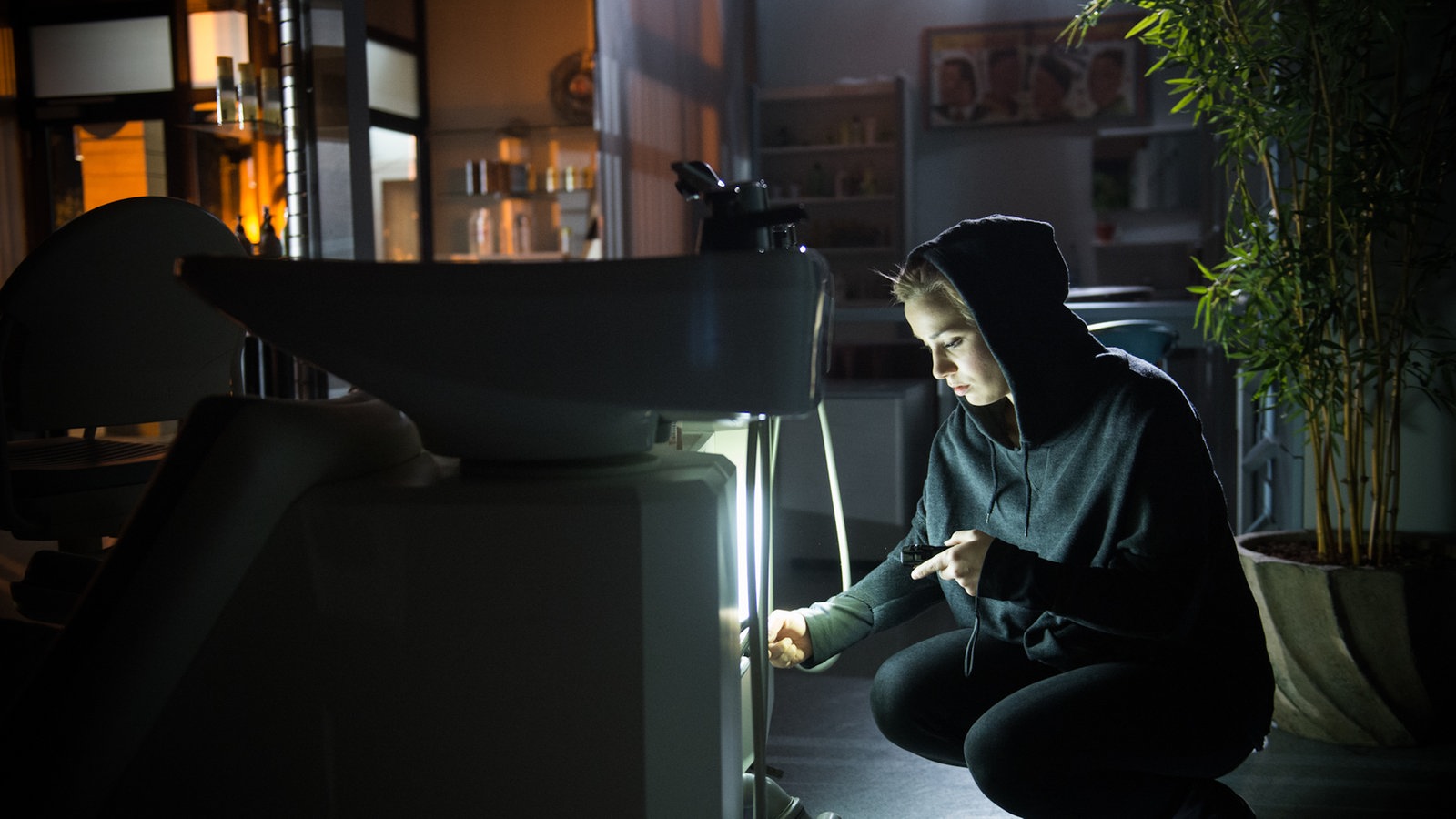 Lea manipuliert im dunklen Friseursalon eine Waschmaschine