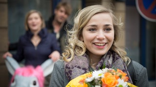 Lea steht mit einem Blumemstrauß vor Tanja und Lotti