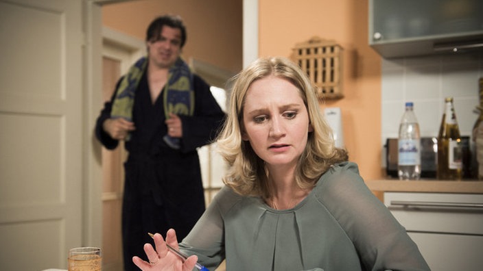Lisa schreibt am Küchentisch, Murat steht im Hintergrund