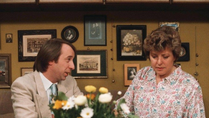 Makler Panowski (Richard Rogler) versucht Helga (Marie-Luise Marjan) zu beweisen, dass alle Arbeiten am Haus in Baldham einwandfrei durchgeführt wurden.