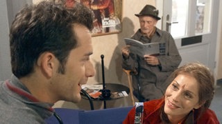 Marion (Ulrike Tscharre) ist aus Indien zurück gekehrt. Mit Onkel Franz (Martin Rickelt, Mitte) im Schlepptau sucht sie Helga – und stößt im Reisebüro auf den attraktiven Alex (Joris Gratwohl).