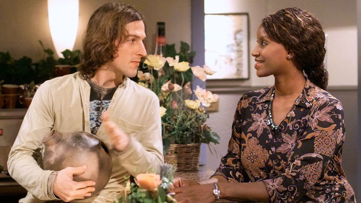 Mary (Liz Baffoe) hat Mikis (Markus Anton) ein afrikanisches Musikinstrument mitgebracht.