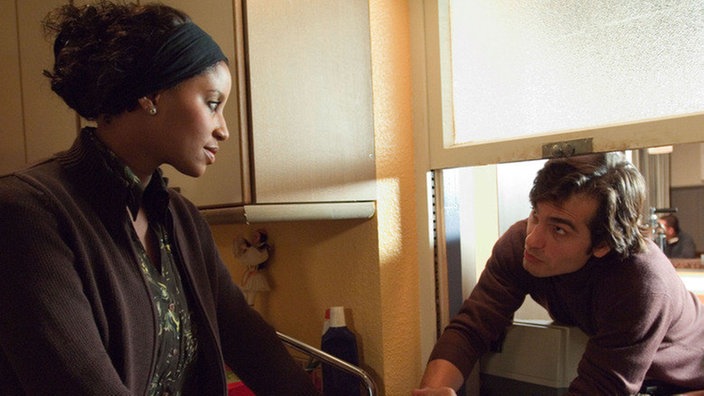 Mary (Liz Baffoe) verabschiedet sich von Vasily (Hermes Hodolides). Sie kann es nicht ertragen, noch länger als Lügnerin hingestellt zu werden und verlässt die Lindenstraße.