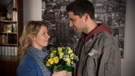 Nina hält einen Blumenstrauß und strahlt Enzo an