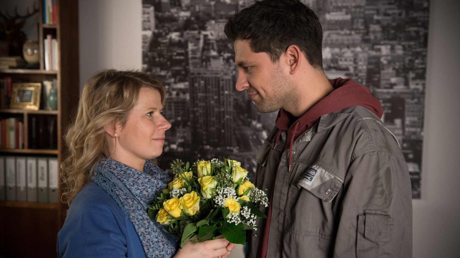 Nina hält einen Blumenstrauß und strahlt Enzo an
