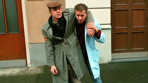 Olli (Willi Herren, rechts) kommt gerade noch im rechten Moment: Hajo (Knut Hinz), der von der Dialyse zurückkehrt, taumelt und wird beinahe von einem Auto erfasst.