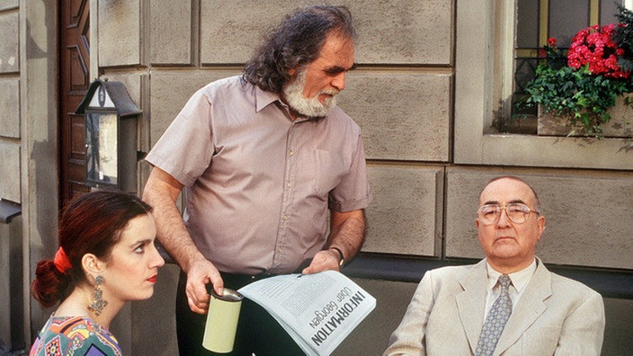 Panaiotis (Kostas Papanastasiou) belästigt mit seiner Sammelaktion Beate (Susanne Gannott) und Dr. Dressler (Ludwig Haas) beim Mittagessen.
