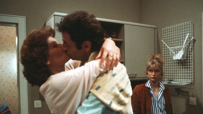 Tanja (Sybille Waury, rechts) muss eifersüchtig mit ansehen, wie ihre Mutter (Monika Woytowicz) und Stefan Nossek (Dietrich Siegl) sich küssen.