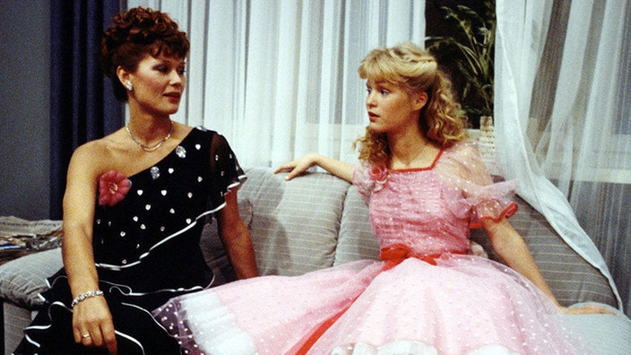 Tanja trägt ein pinkes 50er Jahre Kleid und Henny trägt ein schlichtes schwarzes Kleid