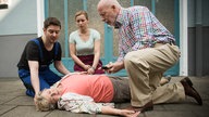 Timo, Lea und Erich kümmern sich um die zusammengebrochene Helga
