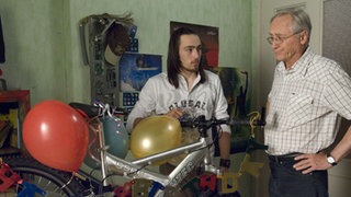 Tom (Johannes Scheit, links) hat nun doch das teure Fahrrad für Kathy gekauft. Hans (Joachim Hermann Luger) hat Zweifel, ob Tom sein Geld richtig angelegt hat.