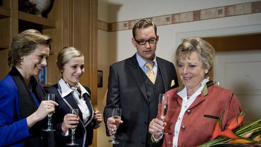 Maja, Lea, Benny und Helga prosten sich in schickem Kostüm mit Sekt zu.