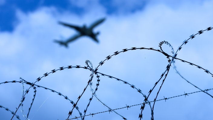 Das Bild zeigt ein Flugzeug das über einen Stacheldraht fliegt.