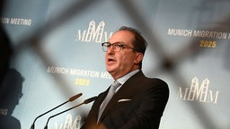 Das Bild zeigt Dobrindt hinter einem unscharfen Zaun