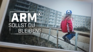 Ein kleines Mädchen sitzt auf einem Holzgeländer eines Spielplatzes im Innenhof einer Plattenbau Siedlung.